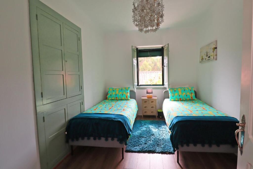 A room with two beds, a window, a small bedside table, and a wardrobe.