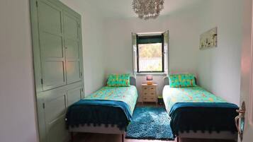 A room with two beds, a window, a small bedside table, and a wardrobe.
