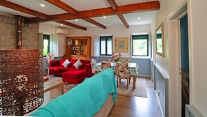 A spacious living area with a red sofa, wooden beams, a fireplace, and a dining table with chairs.