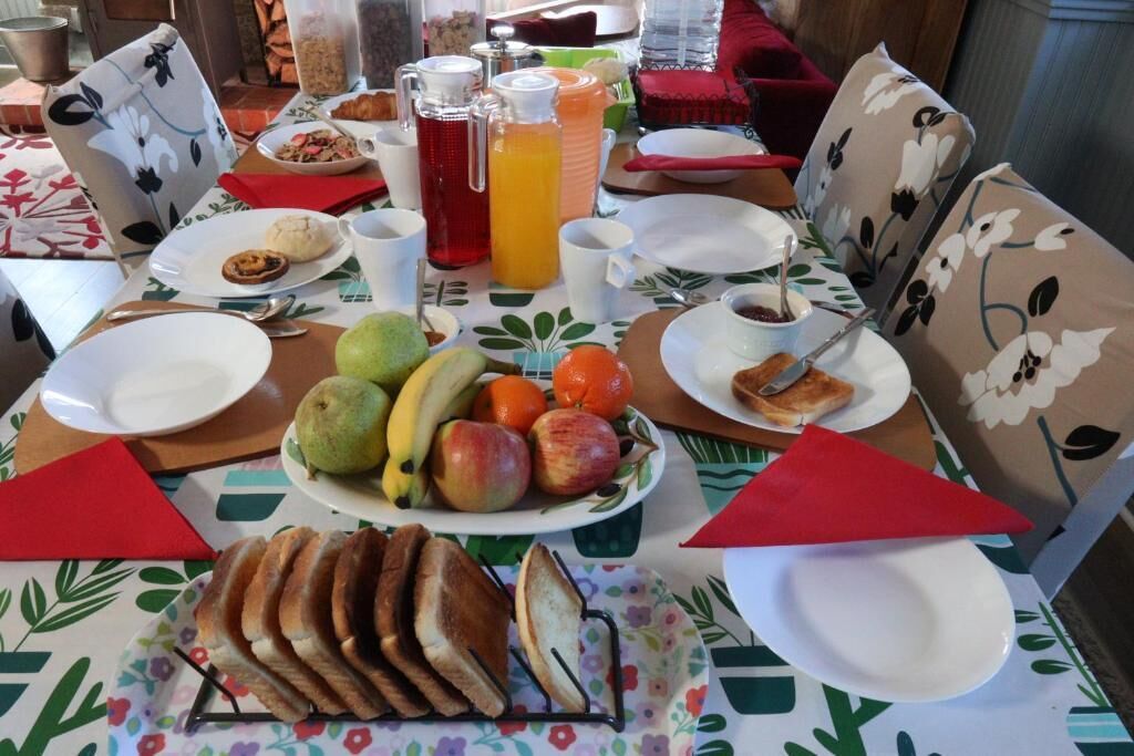 Une table dressée pour le petit-déjeuner, avec des assiettes, des fruits, du pain et des boissons.