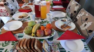 Une table dressée pour le petit-déjeuner, avec des assiettes, des fruits, du pain et des boissons.