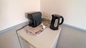 A kitchenette with a coffee maker, a kettle, and a small container on a countertop.