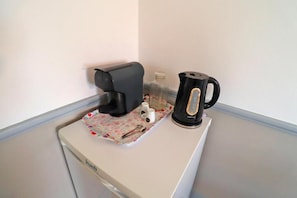 Eine Küchenzeile mit einer Kaffeemaschine, einem Wasserkocher und einer kleinen Aufbewahrungsbox auf einer Arbeitsfläche.