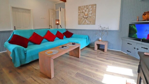 A living room with a teal sofa, red cushions, a wooden coffee table, a television, and a small side table.
