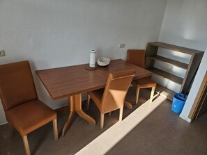 Uma área de refeições com uma mesa de madeira e cadeiras combinando, uma lixeira azul e um banco embutido com prateleiras.