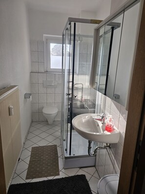 Casa de banho compacta com cabine de duche em vidro, lavatório branco com espelho e sanita.