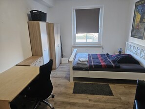 Quarto com cama, escrivaninha, cadeira, radiador e janela.