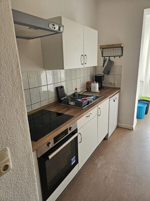 Cozinha compacta com armários brancos, fogão preto e painel de azulejos.