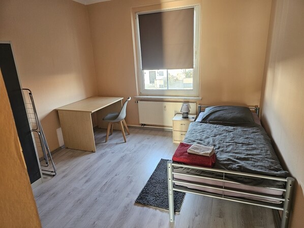 Quarto com cama, escrivaninha, cadeira e radiador.