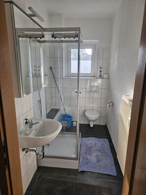 Uma casa de banho compacta com cabine de duche em vidro, lavatório, sanita e janela.