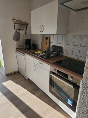 Uma cozinha com armários brancos, bancada de madeira, forno embutido e máquina de café.