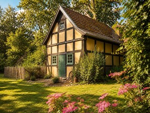 Uma casa tradicional de enxaimel com uma porta verde, rodeada por vegetação exuberante e plantas floridas.