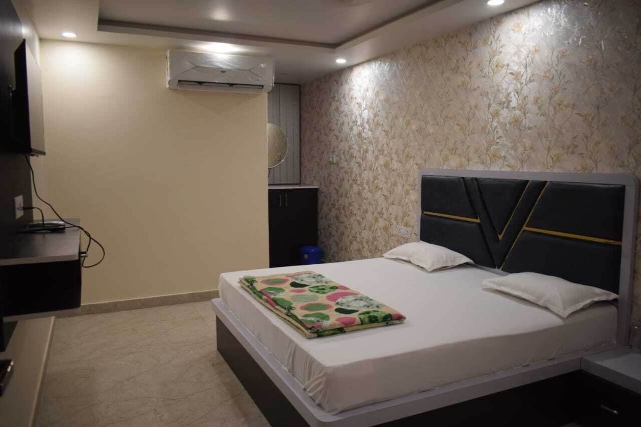 A bedroom with a bed, a bedside table, an air conditioning unit, and a wall-mounted TV.