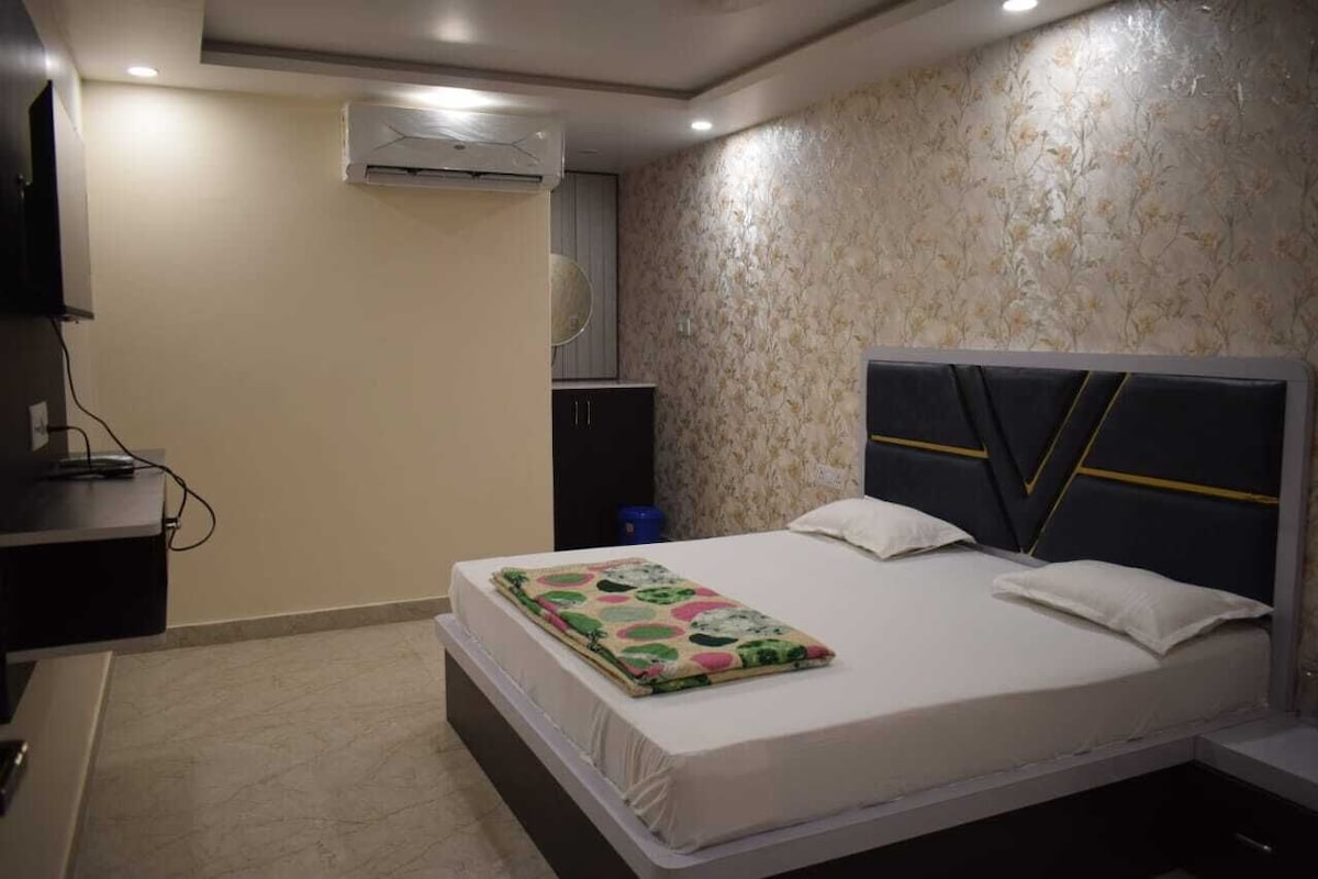 Un dormitorio con cama, mesita de noche, aire acondicionado y televisor montado en la pared.
