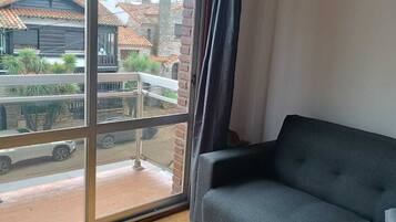 Une pièce dotée d’une grande fenêtre, d’un canapé gris et offrant une vue sur des immeubles et une rue.