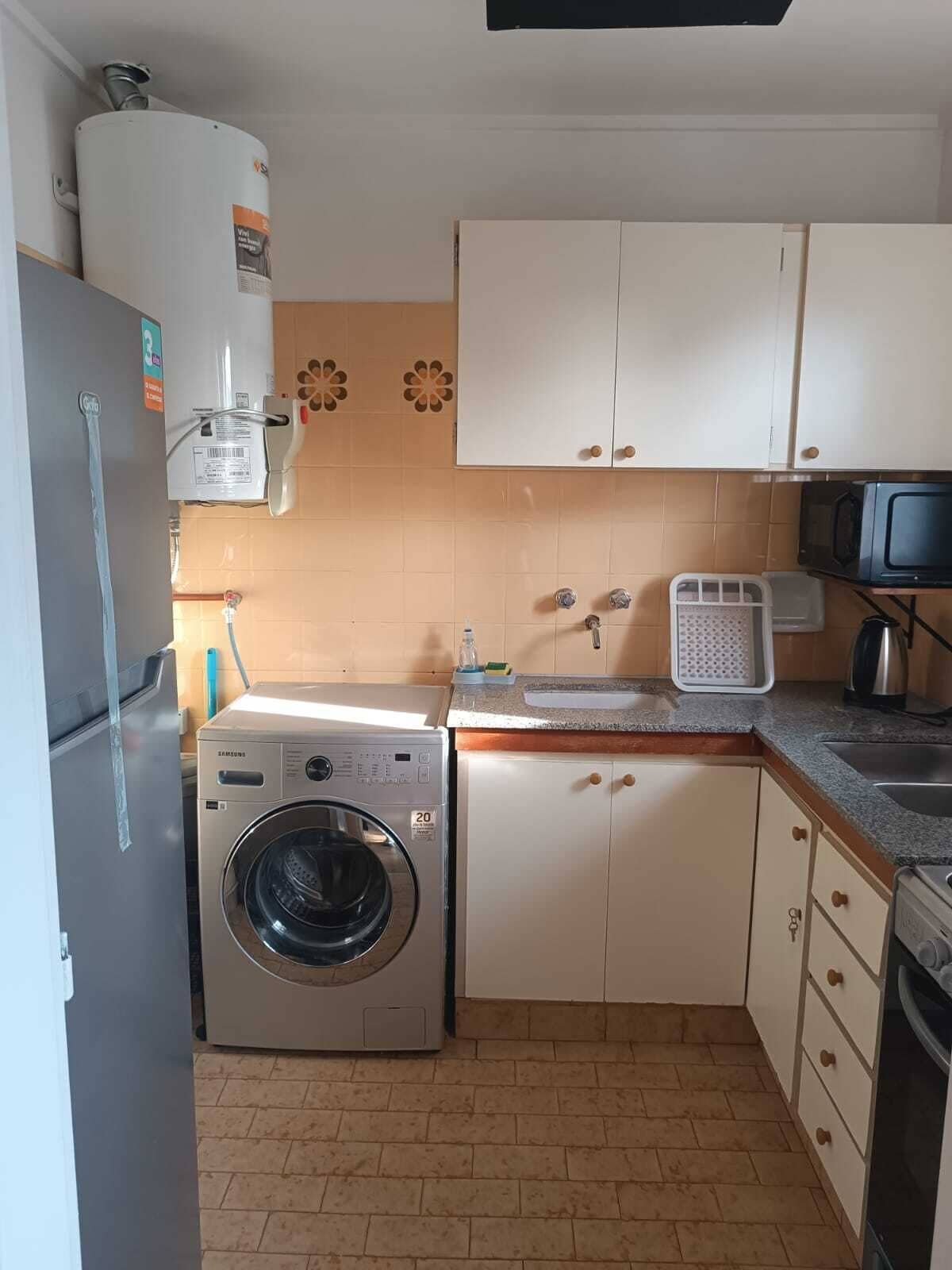 Une cuisine compacte équipée d’un lave-linge, d’un four à micro-ondes et de placards.