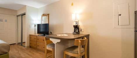 A compact kitchenette with a sink, a coffee maker, a television, and two chairs.