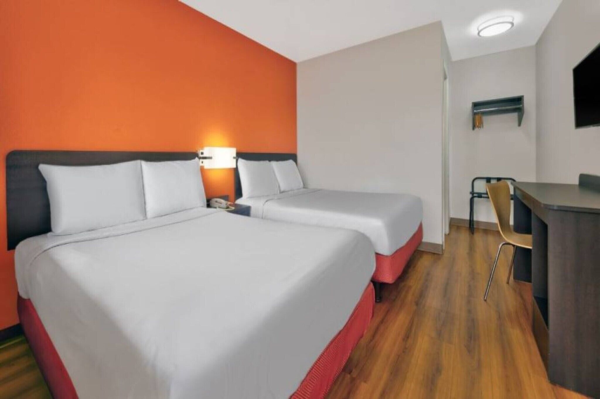 A hotel room with two beds, a desk, and a chair.