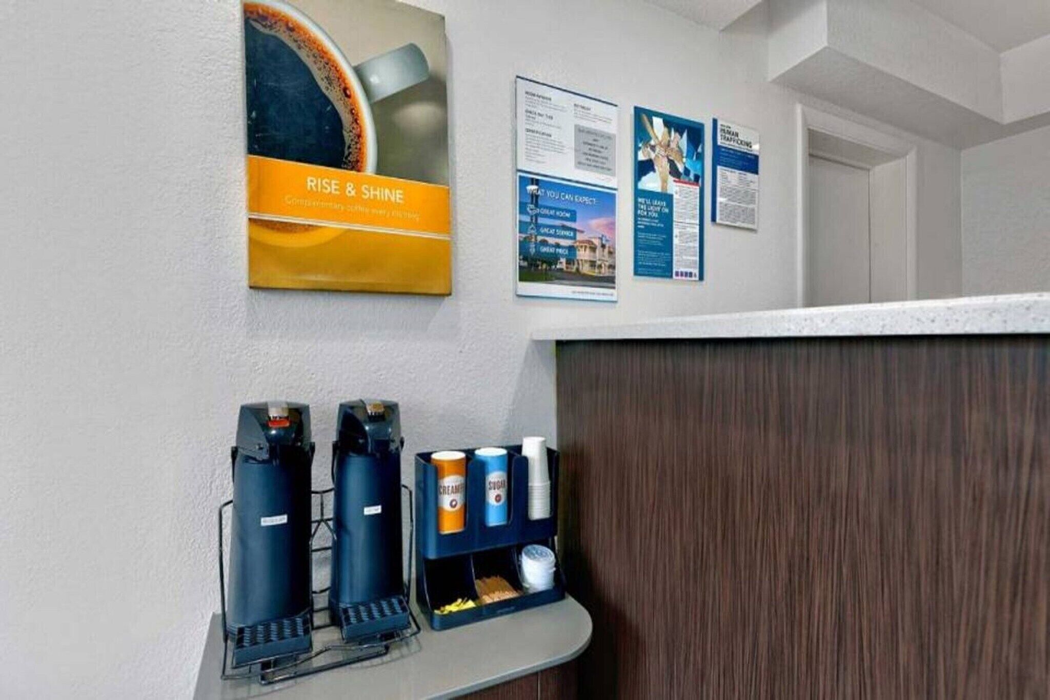 A reception area with a coffee machine, a beverage dispenser, and informational posters on the wall.