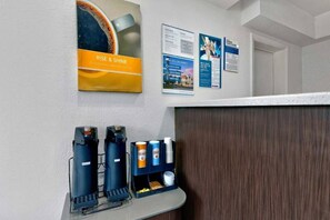 A reception area with a coffee machine, a beverage dispenser, and informational posters on the wall.