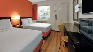 A hotel room with two beds, a desk with a television, a chair, and a window with curtains. - 2 FULL BEDS | Non-Smoking (Columbus GA)