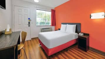 Ein Hotelzimmer mit Bett, Nachttisch, Stuhl, Schreibtisch und einem Fenster mit Vorhängen.