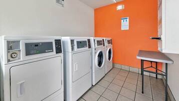 A laundry room with four washing machines, a small table, and an orange wall.