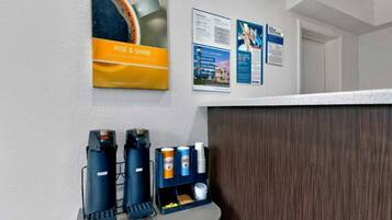 A reception area with a coffee machine, a beverage dispenser, and informational posters on the wall.