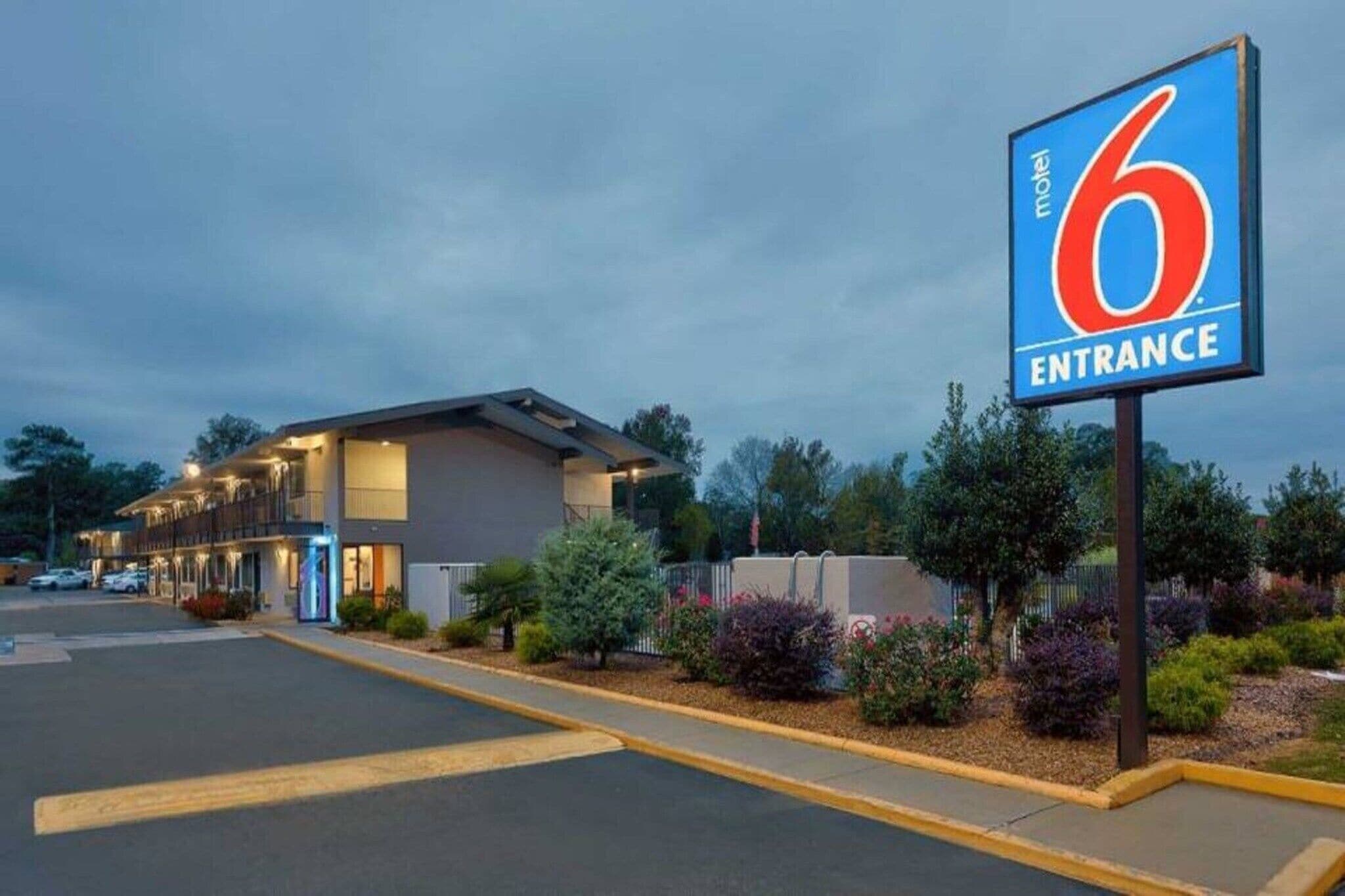 A motel entrance with a large sign, a parking lot, and a building with multiple windows.