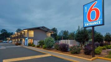 A motel entrance with a large sign, a parking lot, and a building with multiple windows.