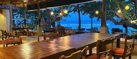 An outdoor dining area with wooden tables and chairs, overlooking a body of water.