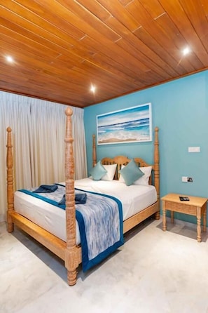 Una cama con dosel con un edredón azul y blanco, una mesita de noche de madera y un cuadro con una playa en la pared.