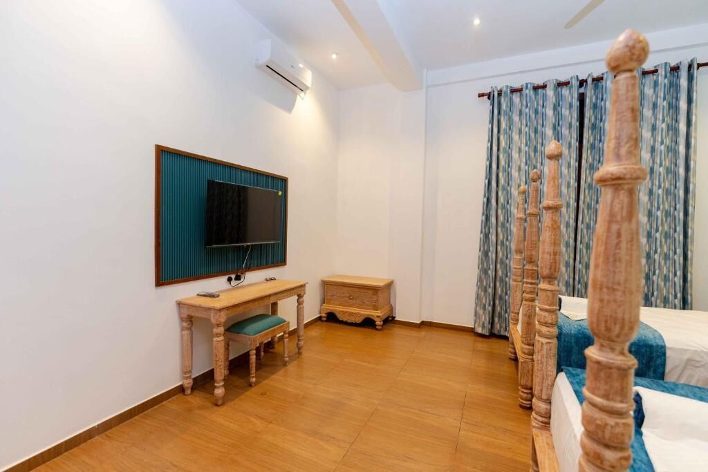 A hotel room with a wooden bed, a TV mounted on the wall, a small wooden desk, and a nightstand.