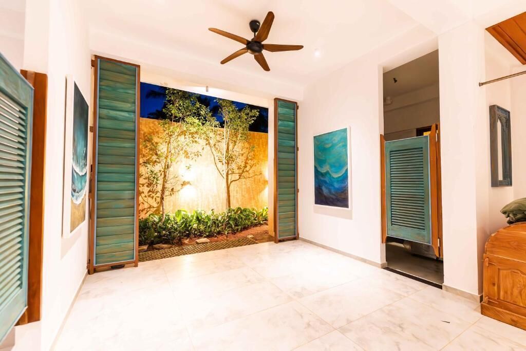 A spacious hallway with a ceiling fan, a view of a garden through a glass door, and artwork on the walls.