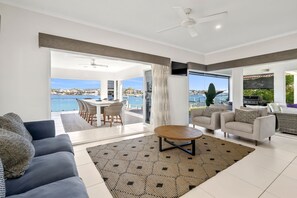 Uma sala de estar ampla com vista para o mar, uma mesa de jantar, sofás e uma mesa de centro.