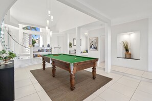 Un salon moderne avec une table de billard, un escalier et une bibliothèque.