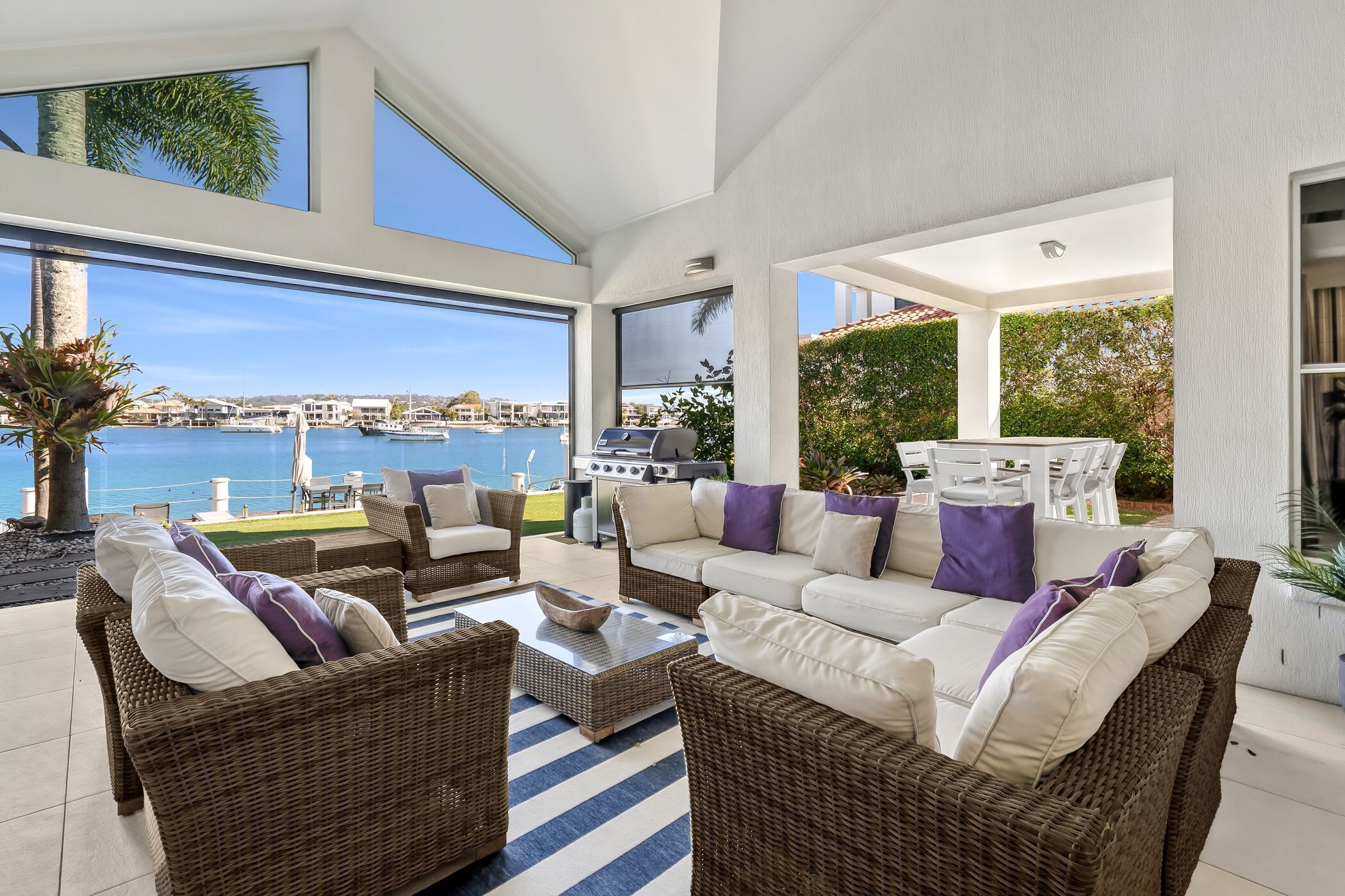 A modern outdoor living space with wicker furniture, a grill, and a view of the marina.