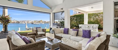 A modern outdoor living space with wicker furniture, a grill, and a view of the marina.