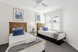 Quarto com duas camas, um ventilador de teto e janela com persianas.
