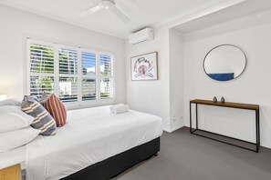 Une chambre moderne avec un lit, une table de chevet, un miroir fixé au mur et une fenêtre avec des stores.