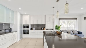 A modern kitchen with white cabinetry, a central island, and pendant lighting. - Waterfront Oasis (Minyama)