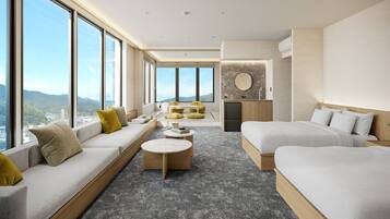 A modern hotel room with a large window, a sofa, a bed, a small kitchen area, and a view of the city.