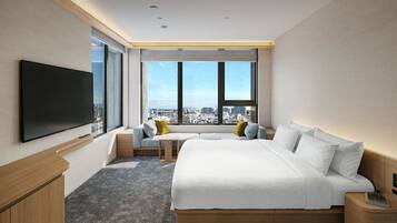 A modern hotel room with a large bed, a TV, a seating area with cushions, and a city view through the windows.