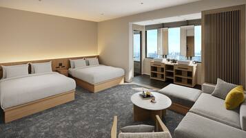 Habitación de hotel con dos camas, un sofá, una mesita y un baño con tocador y espejo.