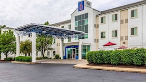 Um hotel com entrada coberta, um grande número '6' e um jardim bem cuidado.
