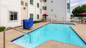 Uma piscina com área de lazer ao redor, incluindo espreguiçadeiras e guarda-sóis, anexa a um edifício com vários andares.