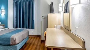 Quarto de hotel com cama, escrivaninha, cadeira, espelho e janela com cortinas.