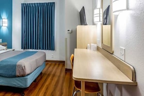 A hotel room with a bed, a desk, a chair, a mirror, and a window with curtains. - 1 Full Bed | Mobility Access Tub, Nsmk (Caseyville)