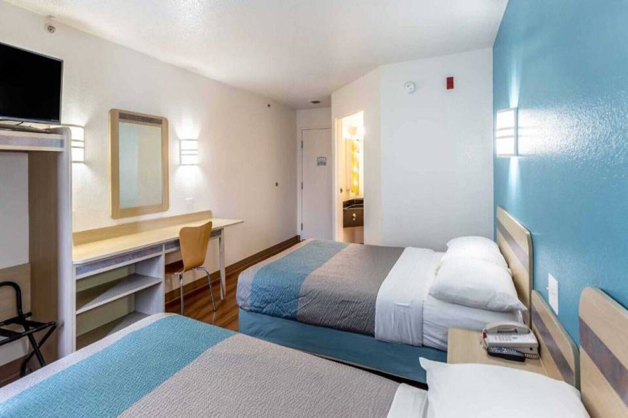 Quarto de hotel com duas camas, uma escrivaninha, uma cadeira e uma televisão.