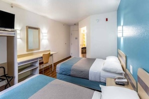 A hotel room with two beds, a desk, a chair, and a TV.